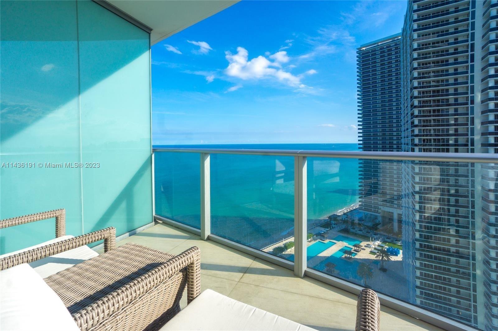 A balcony with wicker lounge chairs overlooks the ocean and a neighboring high-rise building — 4111 S Ocean Dr # 2307, Hollywood FL 33019, HOLLYWOOD, FL