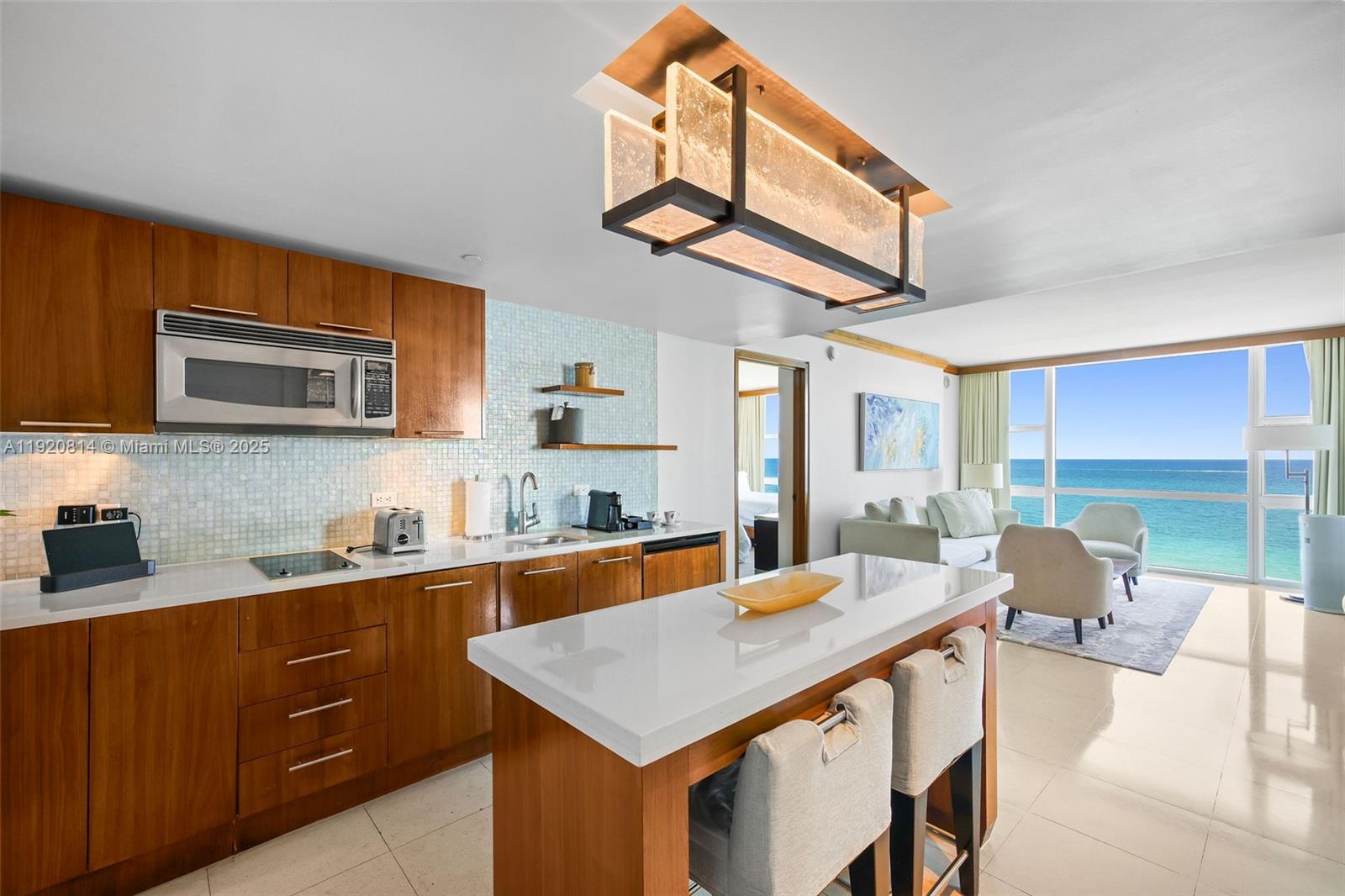 A modern kitchen with wood cabinets and a white island overlooks a coastal living area — 6801 Collins Ave, Miami Beach FL 33141, MIAMI BEACH, FL