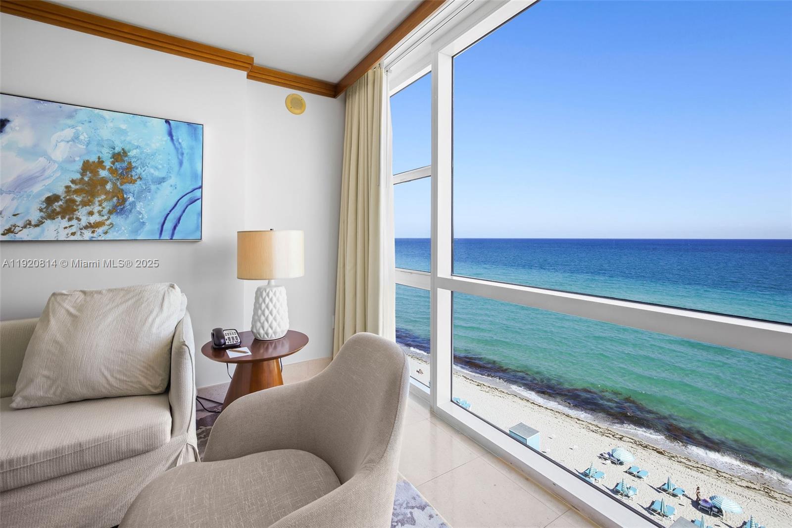 A living area with a beige armchair and ocean view through floor-to-ceiling windows — 6801 Collins Ave, Miami Beach FL 33141, MIAMI BEACH, FL