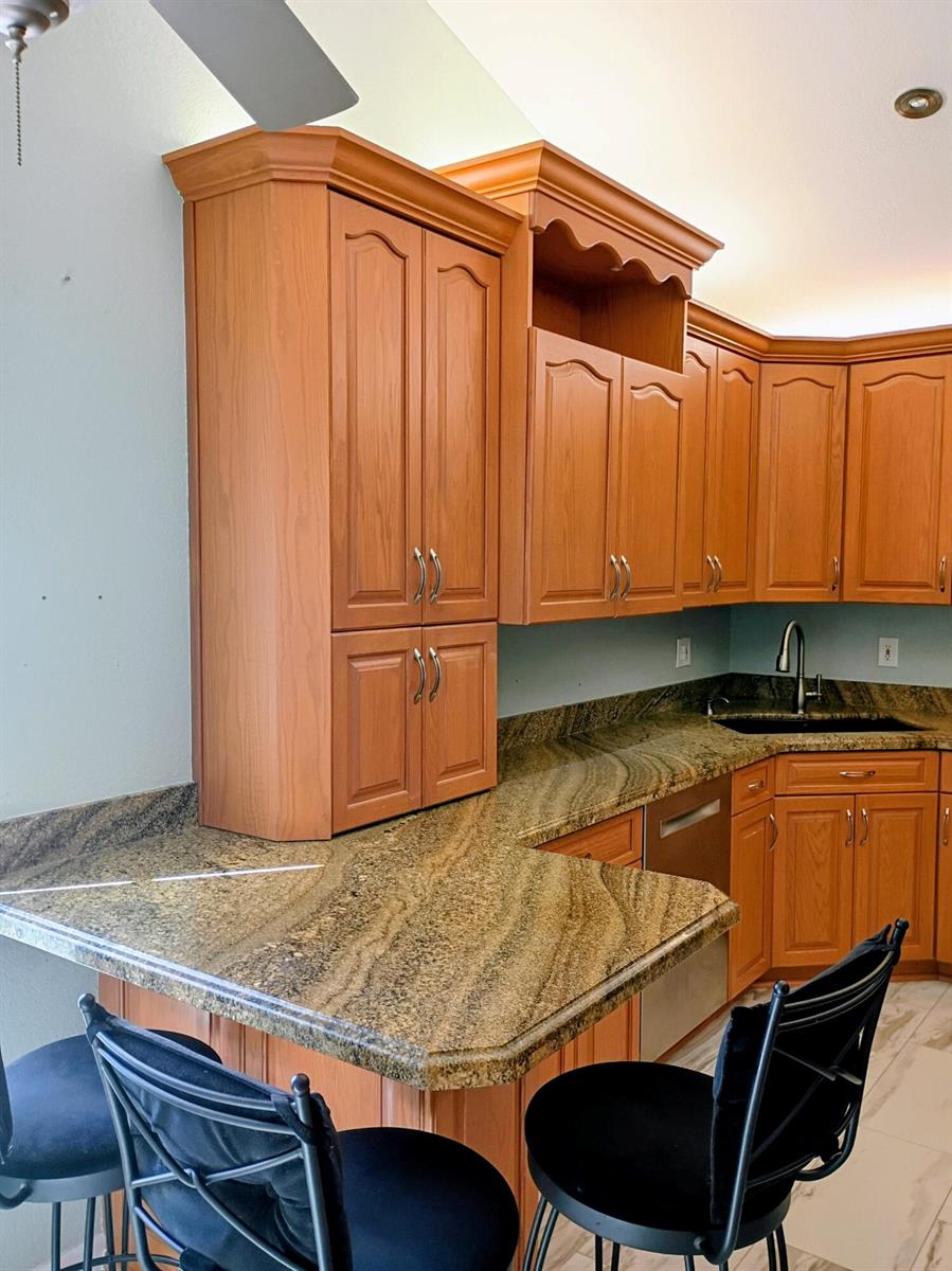 A kitchen features wood cabinets, granite countertops, and a breakfast bar with black stools — 3451 Jog Park Drive, FL 33467, FL