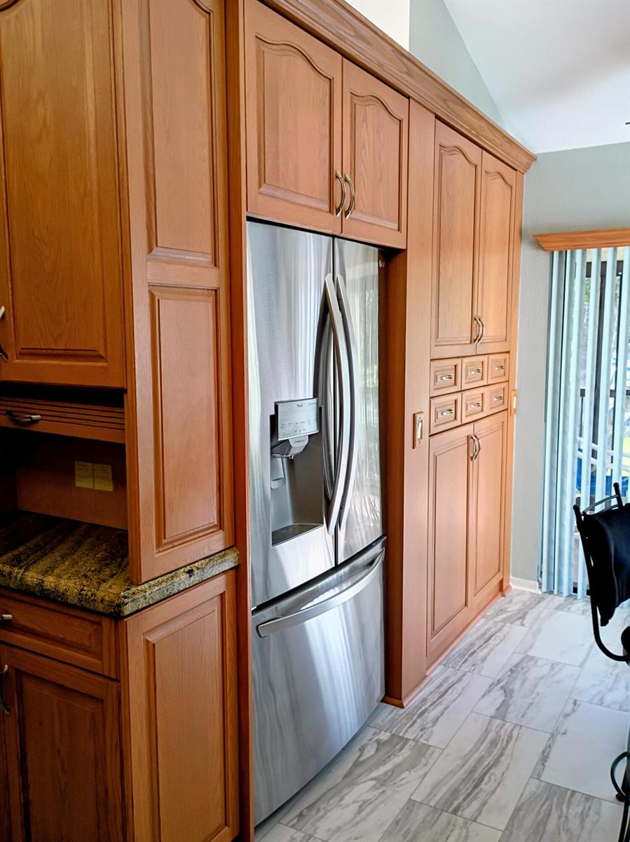 A stainless steel refrigerator is built into oak cabinetry next to a granite countertop — 3451 Jog Park Drive, FL 33467, FL
