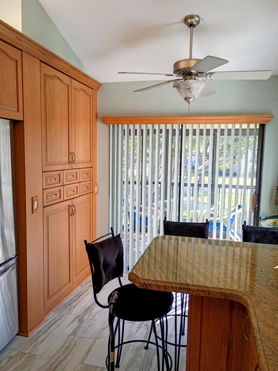 A kitchen dining area features wood cabinets, a granite island, and a sliding glass door — 3451 Jog Park Drive, FL 33467, FL