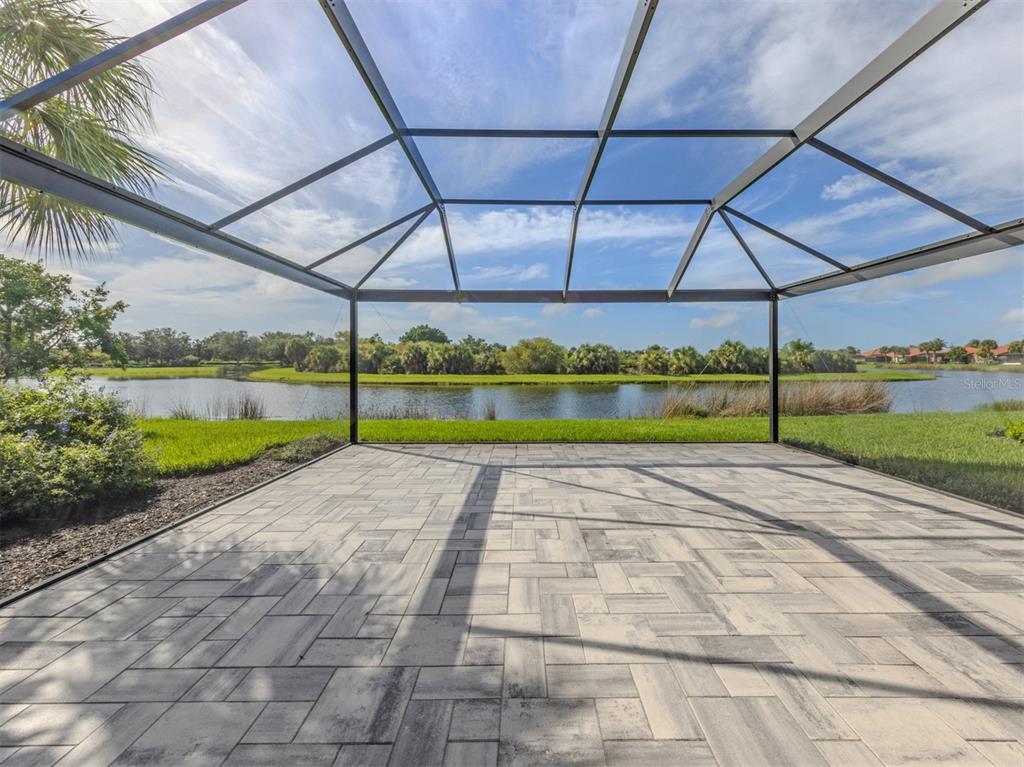 A screened-in patio with gray paver flooring overlooks a lake and grassy landscape — 129 TREVISO COURT, NOKOMIS, FL