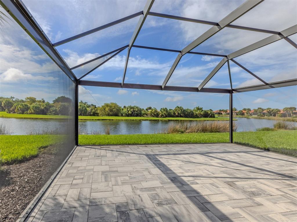 A screened-in patio with paver flooring overlooks a lake and green landscape — 129 TREVISO COURT, NOKOMIS, FL