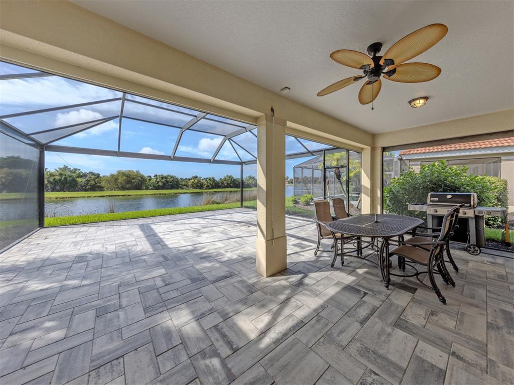 A covered patio features a stone-paver floor, a ceiling fan, and a screened-in water view — 129 TREVISO COURT, NOKOMIS, FL
