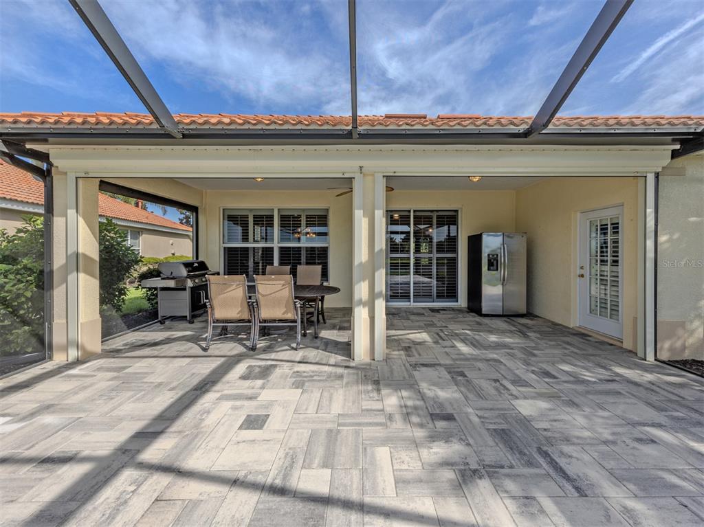 A covered patio features paver flooring, a dining set, a grill, and a refrigerator — 129 TREVISO COURT, NOKOMIS, FL