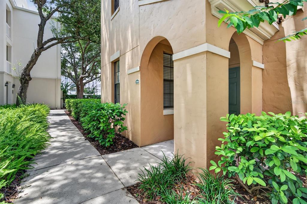 A tan stucco building exterior features arched entryways, a concrete walkway, and surrounding green landscaping — 730 SIENA PALM DRIVE UNIT 104, CELEBRATION, FL