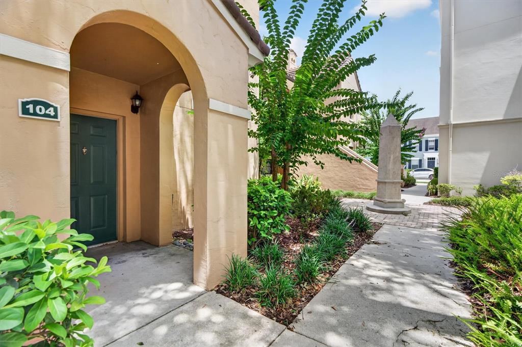 A tan stucco building entrance with a green door and an outdoor stone obelisk — 730 SIENA PALM DRIVE UNIT 104, CELEBRATION, FL