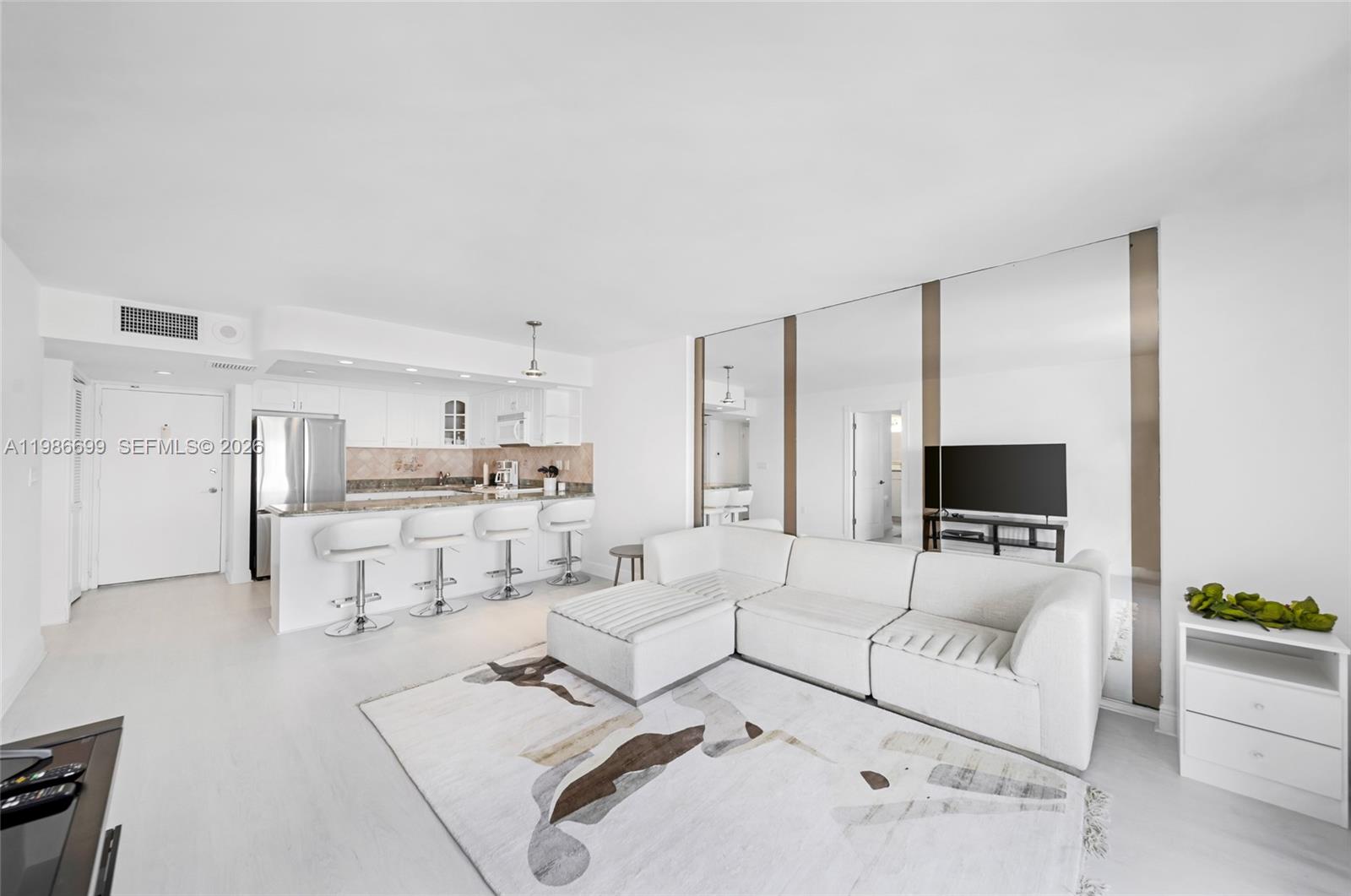 A white living room features a sectional sofa, a patterned rug, and an open kitchen — 465 Ocean Dr # 1102, Miami Beach FL 33139, MIAMI BEACH, FL