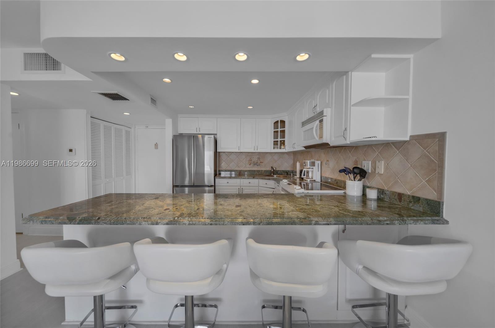 A kitchen features white cabinets, granite countertops, and four white bar stools at a counter — 465 Ocean Dr # 1102, Miami Beach FL 33139, MIAMI BEACH, FL