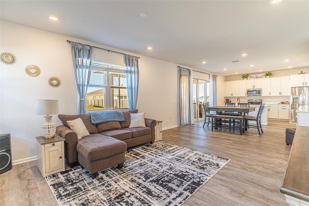 An open-concept living and dining area features a brown sectional, area rug, and white kitchen — 1123 SUGARWOOD STREET, DAVENPORT, FL