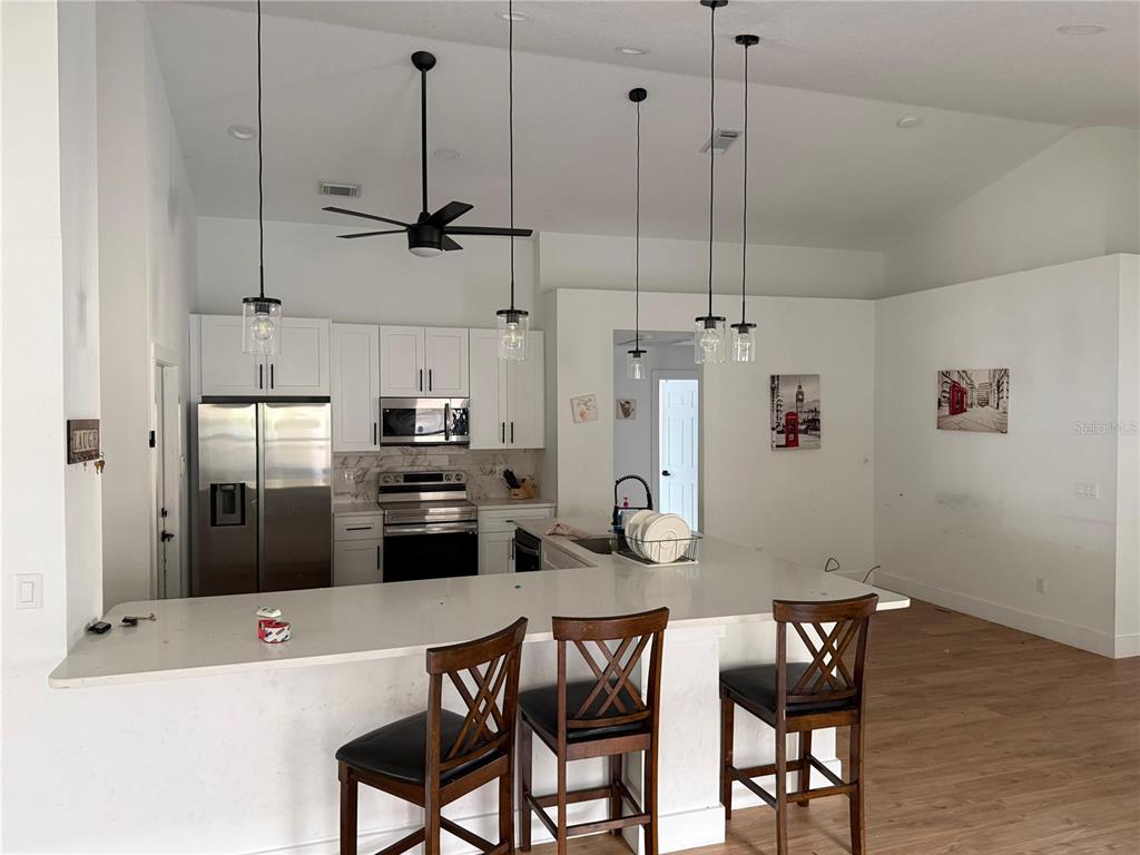 A kitchen features white cabinets, stainless steel appliances, a quartz island, and three pendant lights — 15909 GREEN COVE BOULEVARD, CLERMONT, FL