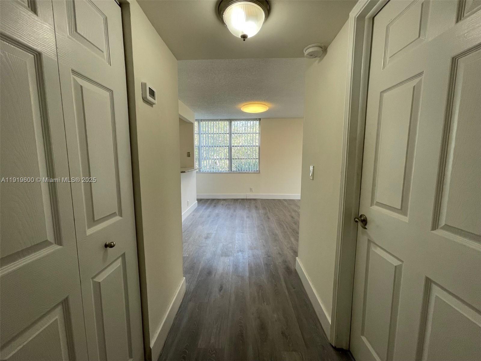 A hallway with wood-look flooring leads into a living area with a large window — 9471 Evergreen Pl # 401, Davie FL 33324, DAVIE, FL