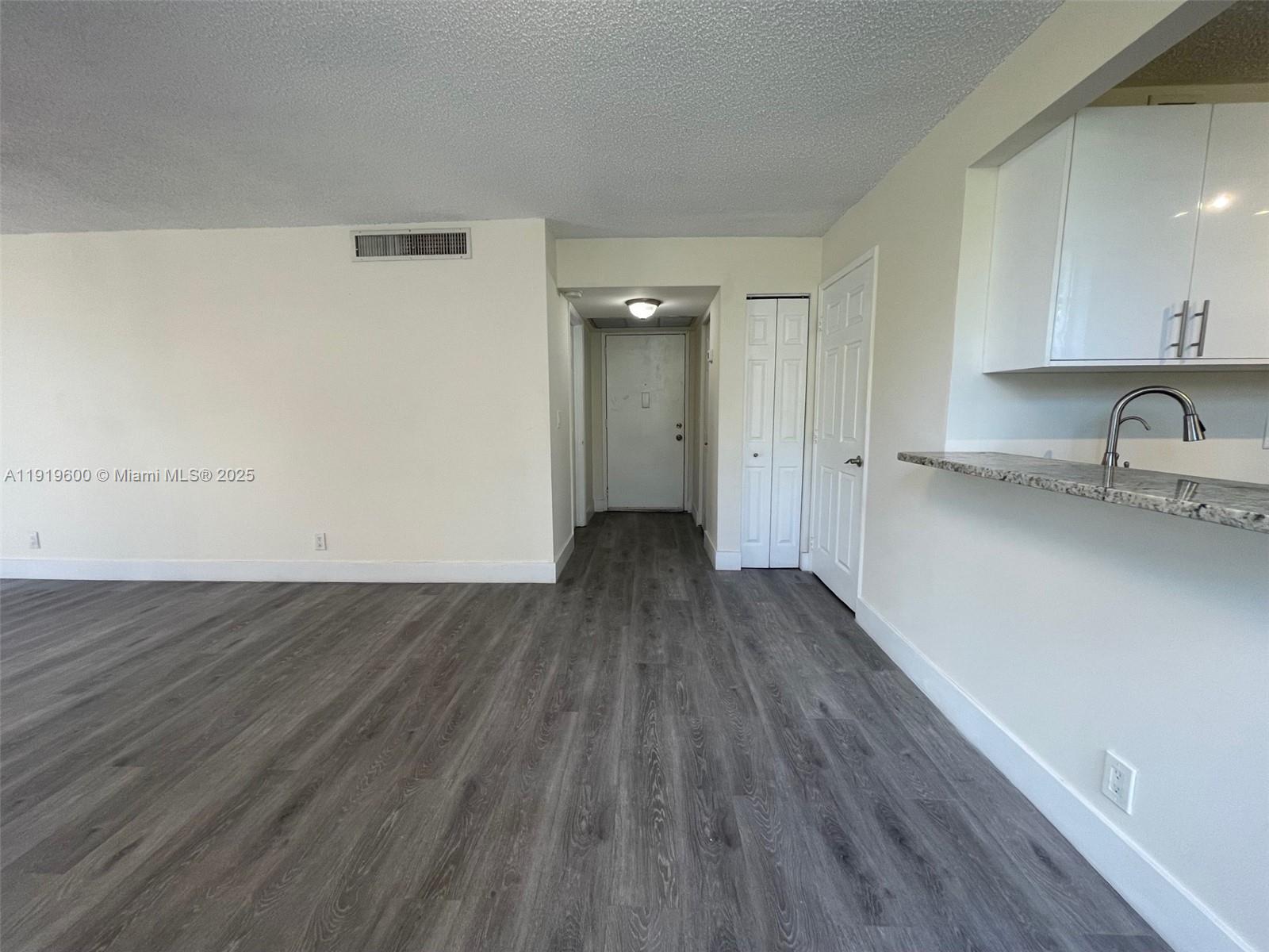 A living area with gray wood-look flooring, white walls, and a kitchen pass-through counter — 9471 Evergreen Pl # 401, Davie FL 33324, DAVIE, FL
