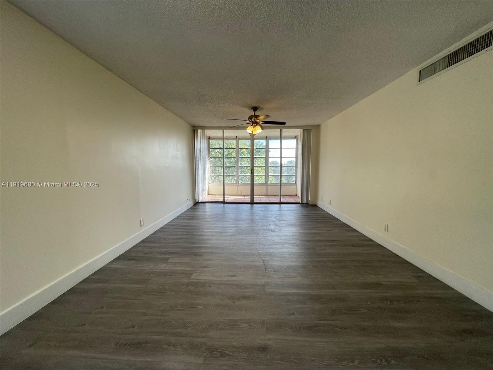 An empty living room features wood-look flooring, cream walls, and a sliding glass door — 9471 Evergreen Pl # 401, Davie FL 33324, DAVIE, FL