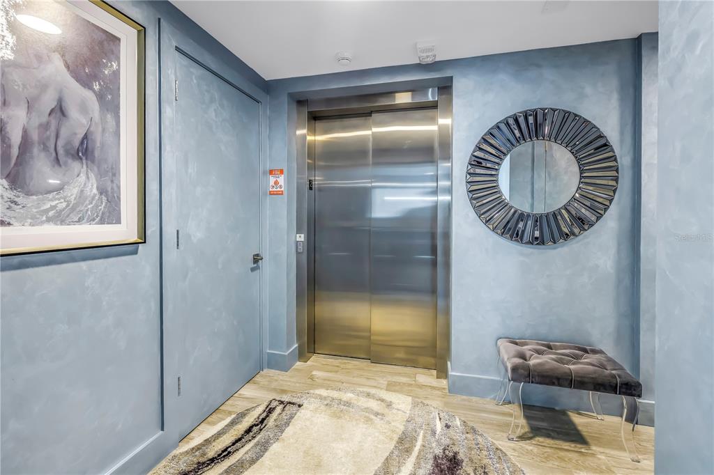 An elevator lobby features blue faux-finished walls, a circular mirror, a tufted bench, and artwork — 19816 GULF BOULEVARD UNIT 201, INDIAN SHORES, FL