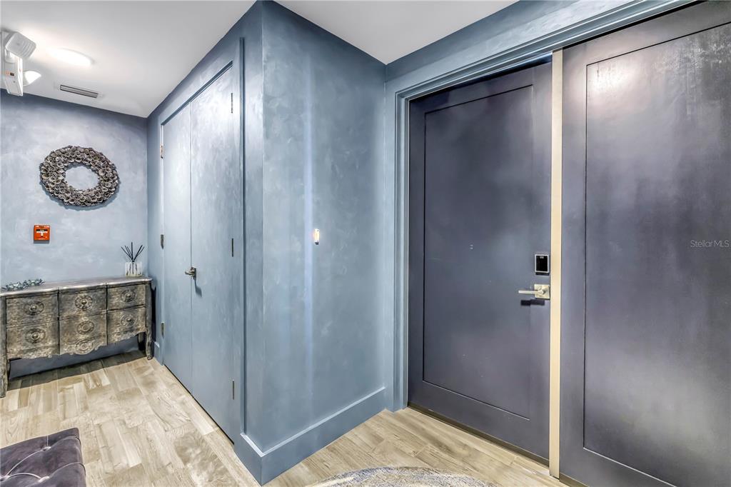 A blue-walled entryway features a dark door, a wooden dresser, and light wood flooring — 19816 GULF BOULEVARD UNIT 201, INDIAN SHORES, FL