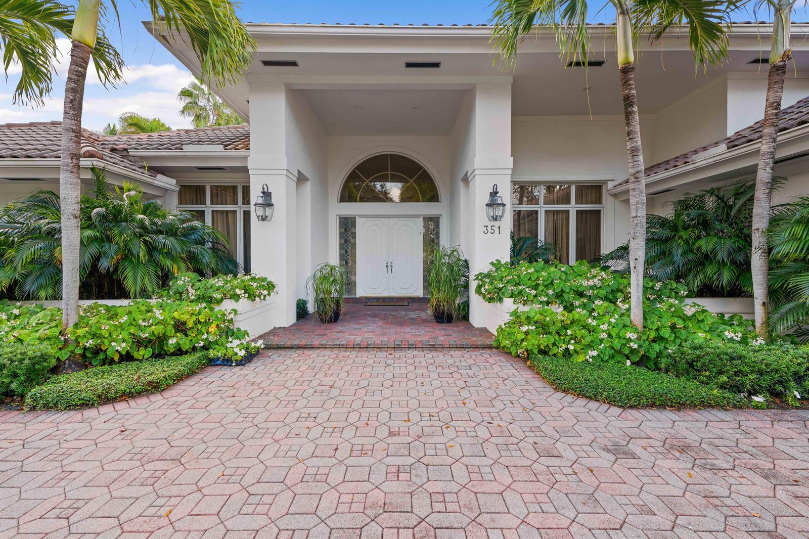 The exterior of a white house features a paved driveway, arched entryway, and palm trees — 351 Eagle Drive, Jupiter FL 33477, JUPITER, FL