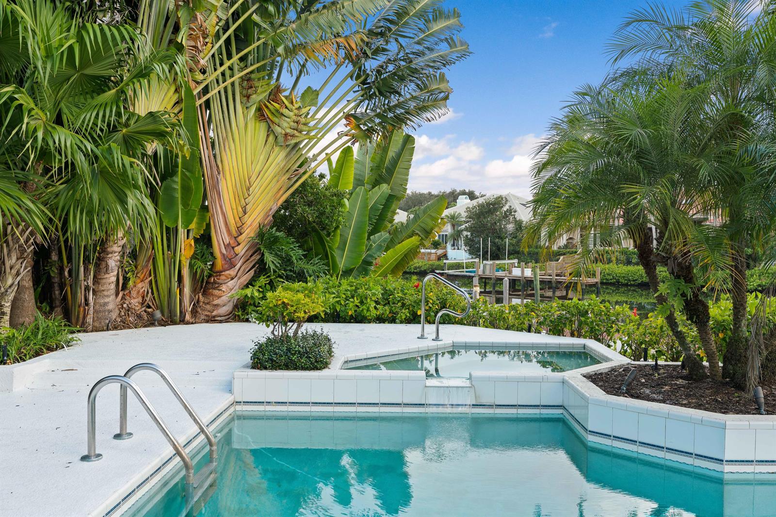A swimming pool and spa overlook a canal with a wooden dock and tropical landscaping — 351 Eagle Drive, Jupiter FL 33477, JUPITER, FL