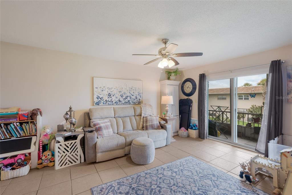 A living room features a light-colored sofa, tiled floors, a ceiling fan, and sliding glass doors — 2727 75TH STREET W UNIT 7A11, BRADENTON, FL