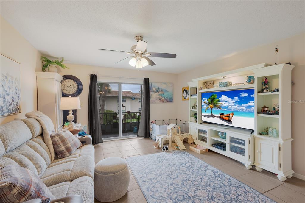 A living room features a beige sofa, a large entertainment center, and a sliding glass door — 2727 75TH STREET W UNIT 7A11, BRADENTON, FL