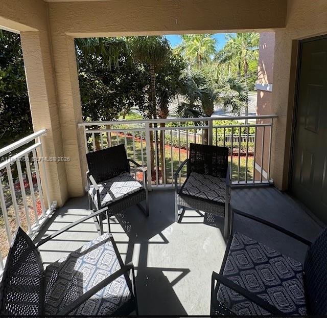 A covered balcony features four wicker chairs with patterned cushions overlooking a landscaped outdoor area — 6434 Emerald Dunes Dr # 304, West Palm Beach FL 33411, WEST PALM BEACH, FL