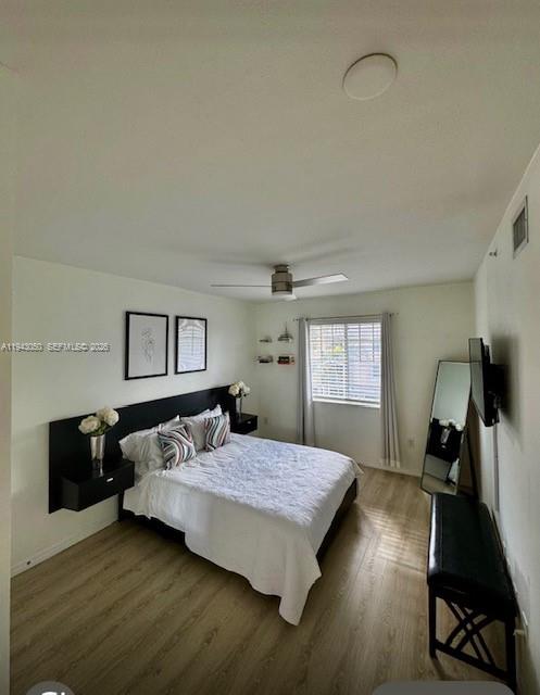 A bedroom features a bed with a black headboard, wood-look flooring, and a ceiling fan — 6434 Emerald Dunes Dr # 304, West Palm Beach FL 33411, WEST PALM BEACH, FL