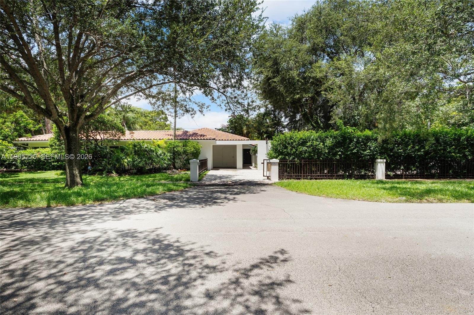 A single-story house with a tiled roof sits behind a gated driveway and mature trees — 5810 Maggiore St # 0, Coral Gables FL 33146, CORAL GABLES, FL