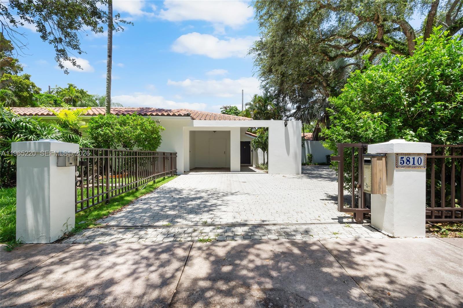 A white house with a tiled roof features a gated driveway and a covered carport — 5810 Maggiore St # 0, Coral Gables FL 33146, CORAL GABLES, FL