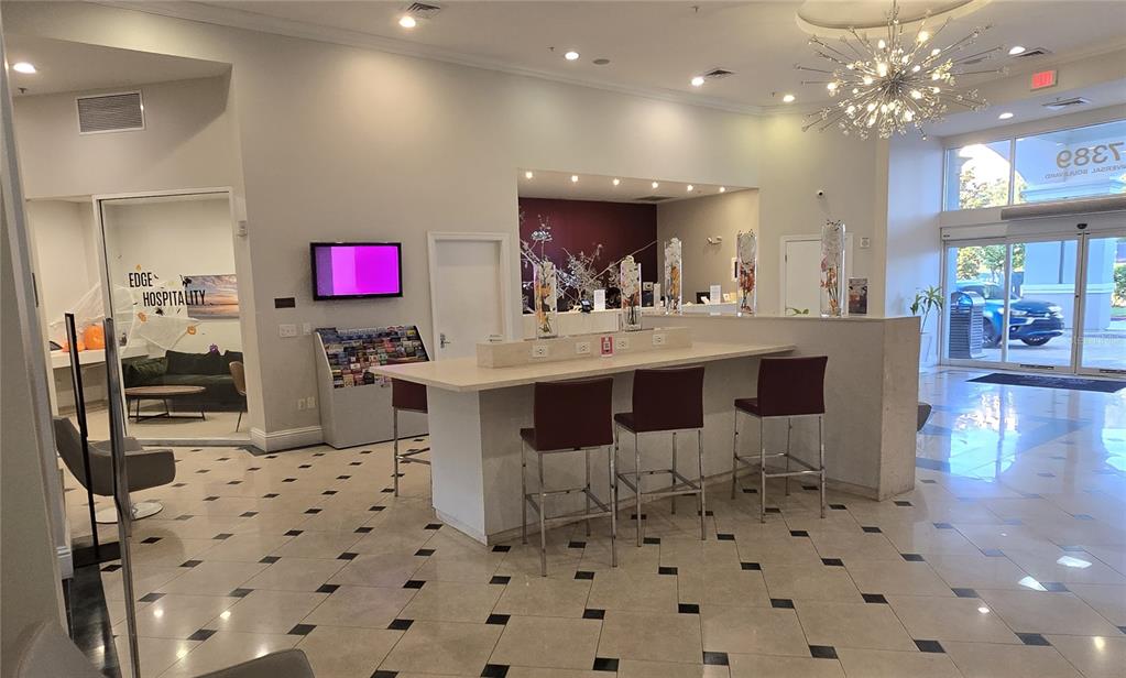 A hotel lobby features a central bar-height table with stools, tile flooring, and glass doors — 7395 UNIVERSAL BOULEVARD UNIT 502, ORLANDO, FL