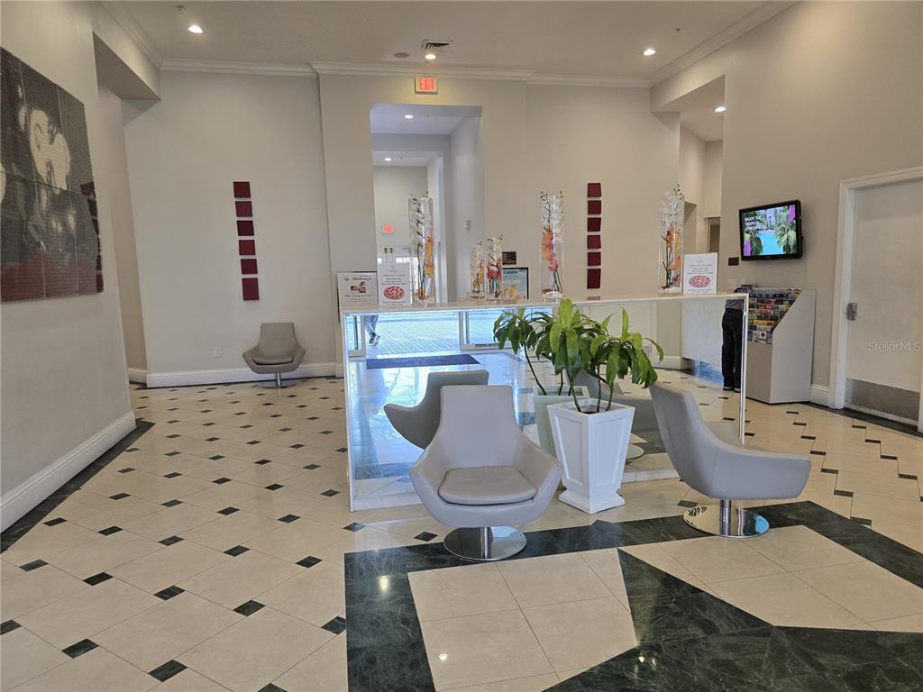 A modern lobby features a white reception desk, gray swivel chairs, and tiled flooring — 7395 UNIVERSAL BOULEVARD UNIT 502, ORLANDO, FL