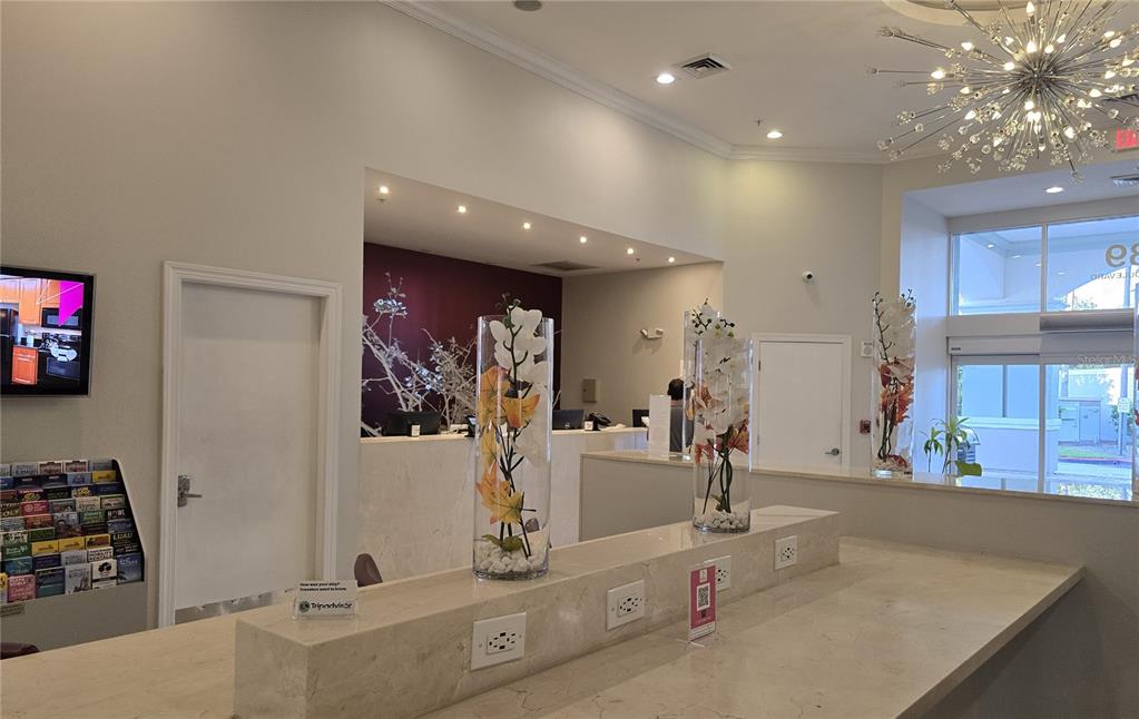 A hotel lobby features a long stone reception desk with floral centerpieces and a chandelier — 7395 UNIVERSAL BOULEVARD UNIT 502, ORLANDO, FL