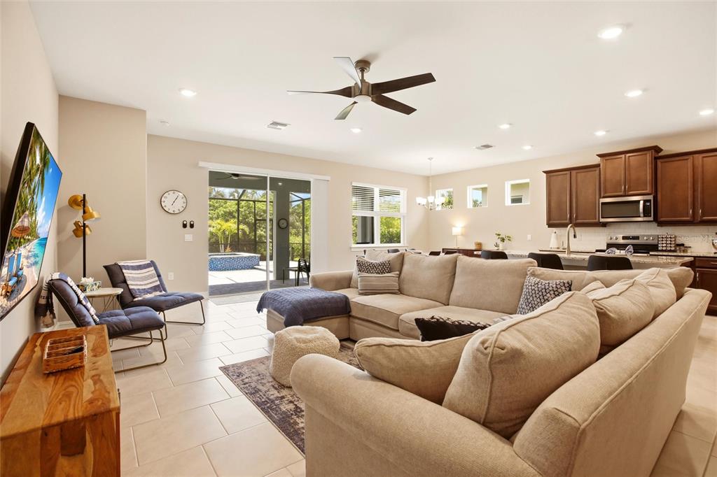 A living room with a sectional sofa, tile floors, and an open kitchen with dark cabinets — 844 HEATHER LAKE AVENUE, CAPE CORAL, FL