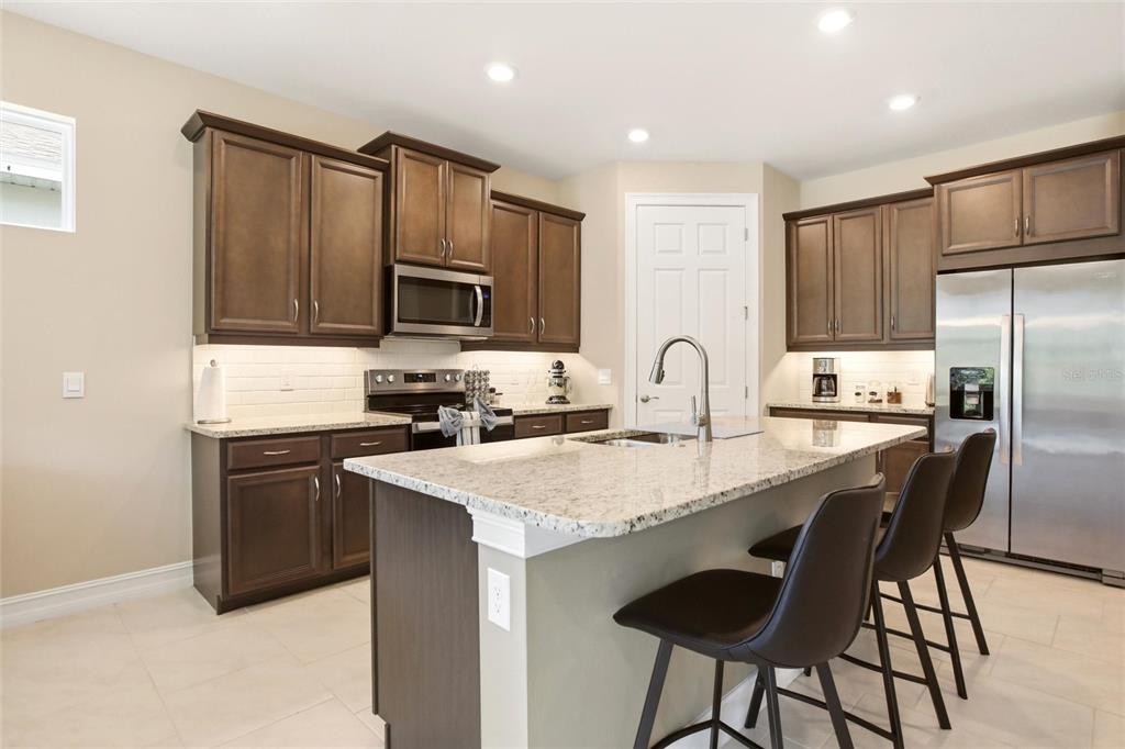 A kitchen with dark wood cabinets, granite countertops, a center island, and stainless steel appliances — 844 HEATHER LAKE AVENUE, CAPE CORAL, FL