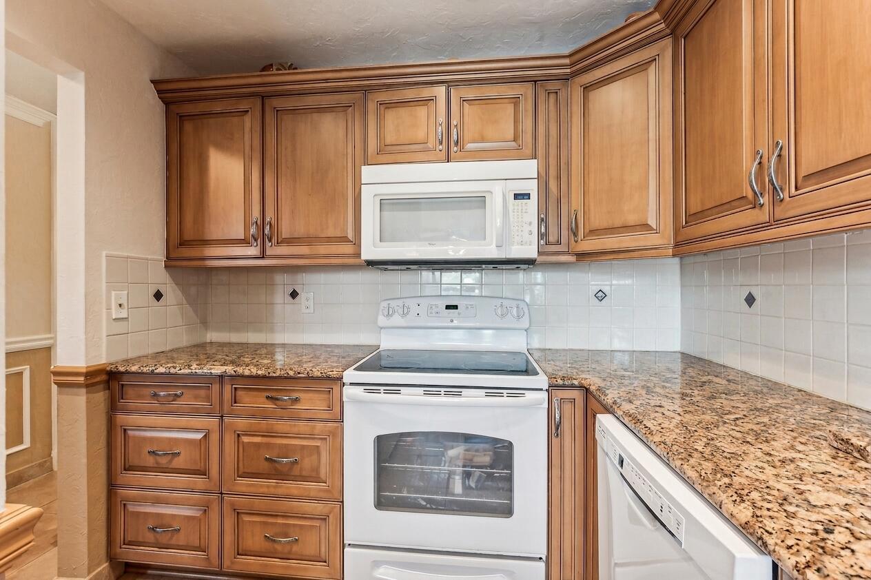 A kitchen features wood cabinets, granite countertops, a white stove, and a white microwave — 1051 Orange Terrace # 103, Delray Beach FL 33445, DELRAY BEACH, FL
