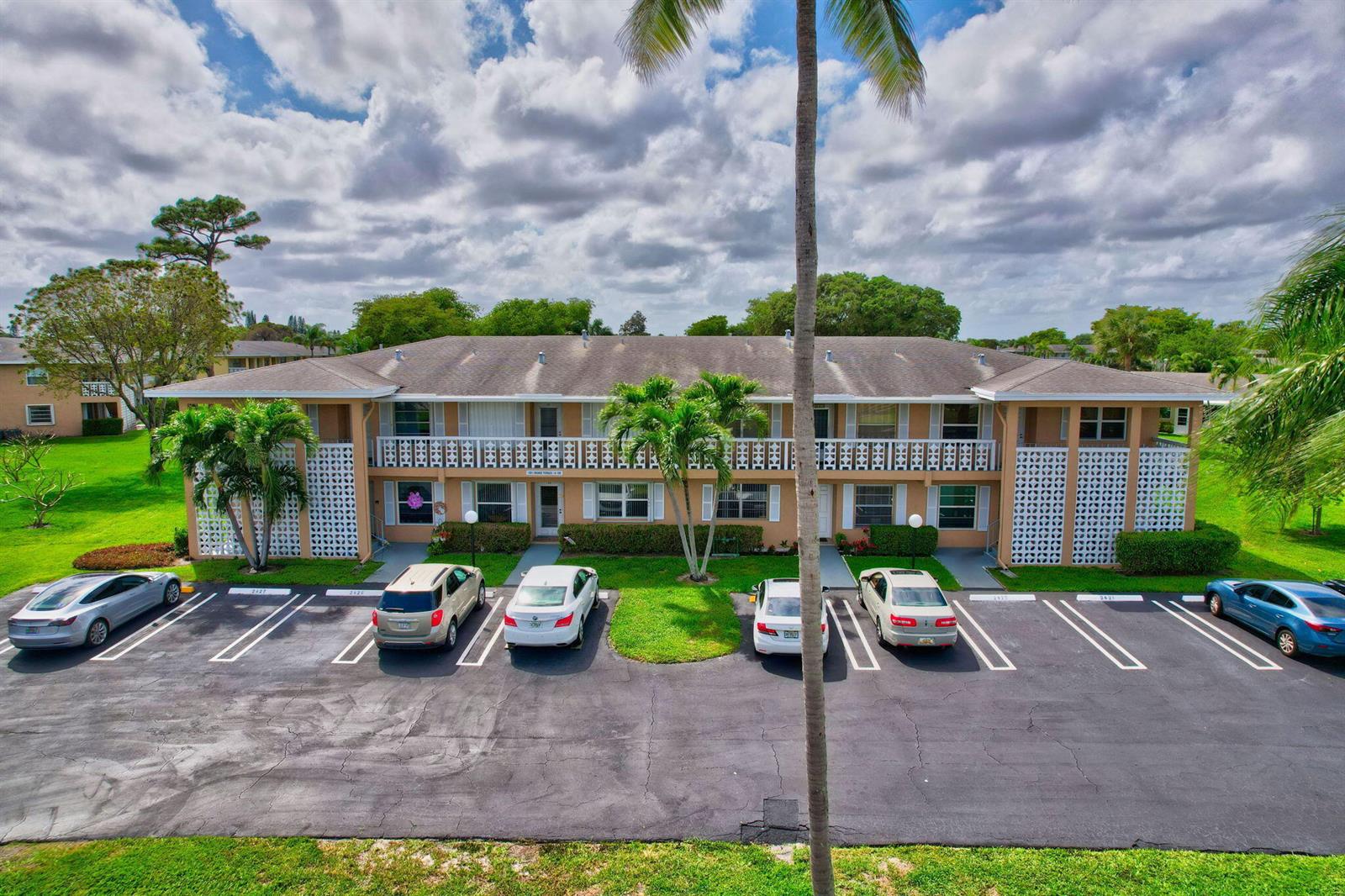 A two-story apartment building with a parking lot and palm trees under a cloudy sky — 1051 Orange Terrace # 103, Delray Beach FL 33445, DELRAY BEACH, FL
