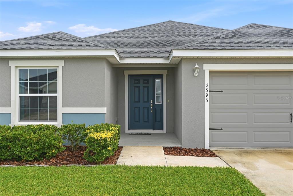 A single-story house exterior features gray stucco walls, a blue front door, and a garage — 2595 SAN MARCO WAY, WINTER HAVEN, FL