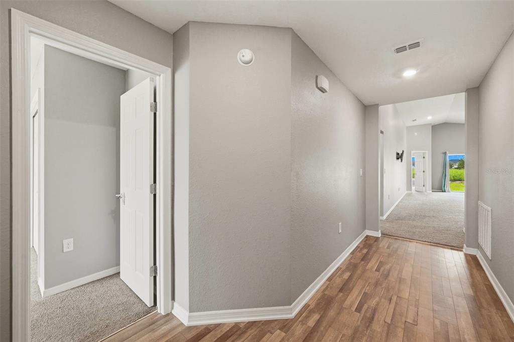 A hallway with wood-look flooring leads to a carpeted living area with a glass door — 2595 SAN MARCO WAY, WINTER HAVEN, FL
