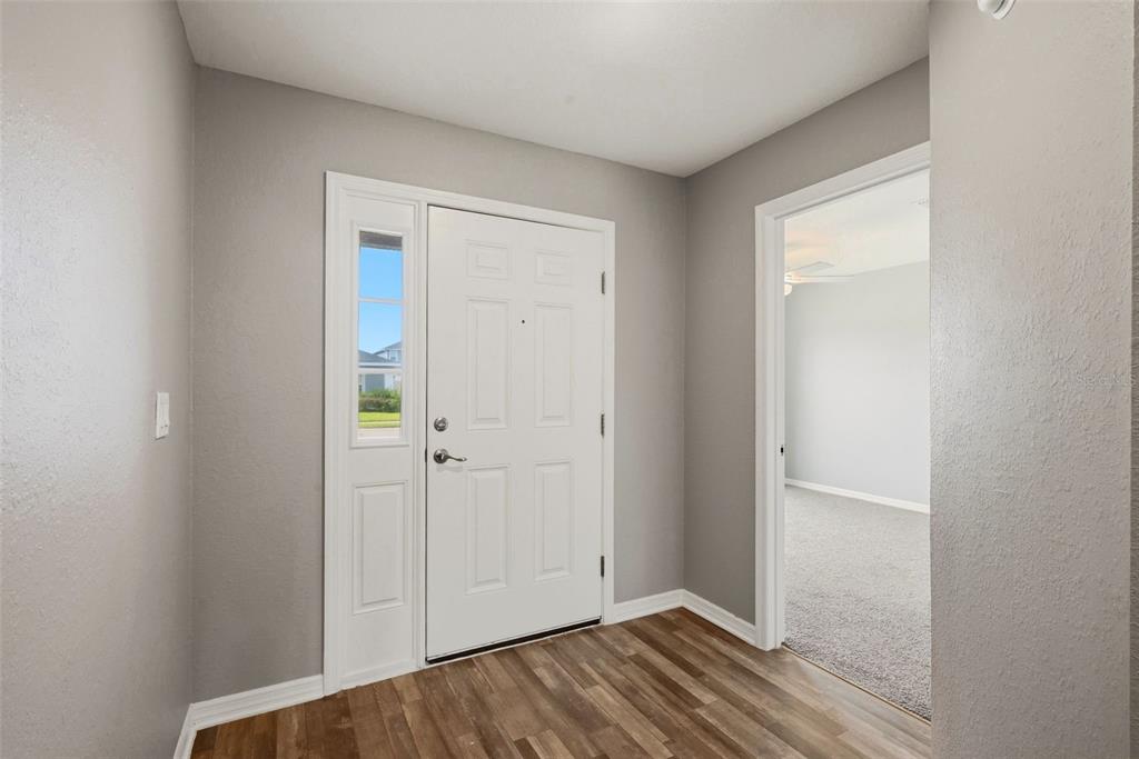 An entryway features a white front door with a sidelight, gray walls, and wood-look flooring — 2595 SAN MARCO WAY, WINTER HAVEN, FL