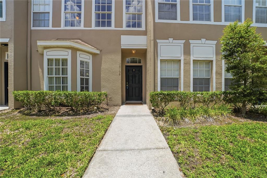A concrete walkway leads to the front entrance of a multi-story tan townhouse — 10106 BELLEVILLE PLACE, TAMPA, FL