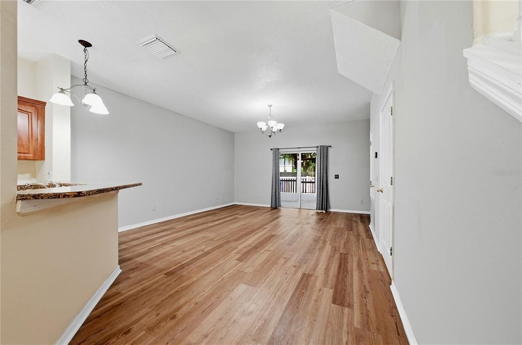 An empty room with light wood-look flooring, a chandelier, and a sliding glass door — 10106 BELLEVILLE PLACE, TAMPA, FL