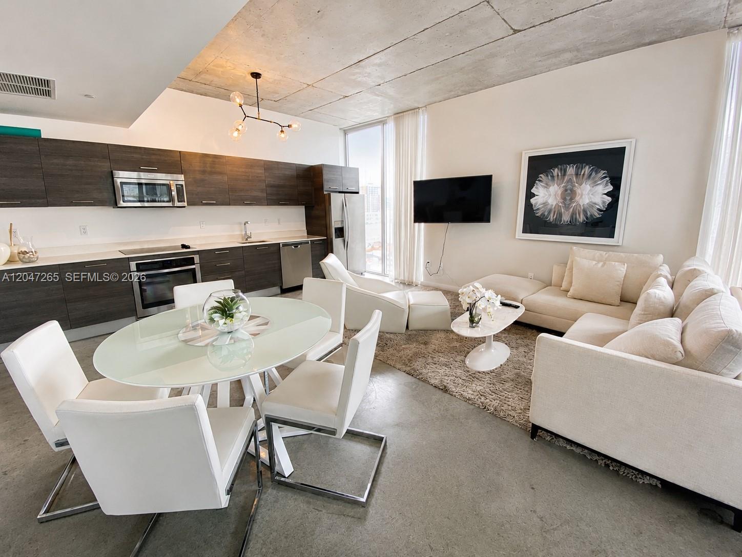 An open-concept living area features a modern kitchen, dining set, and sofa on concrete floors — 151 SE 1st St # 1602, Miami FL 33131, MIAMI, FL