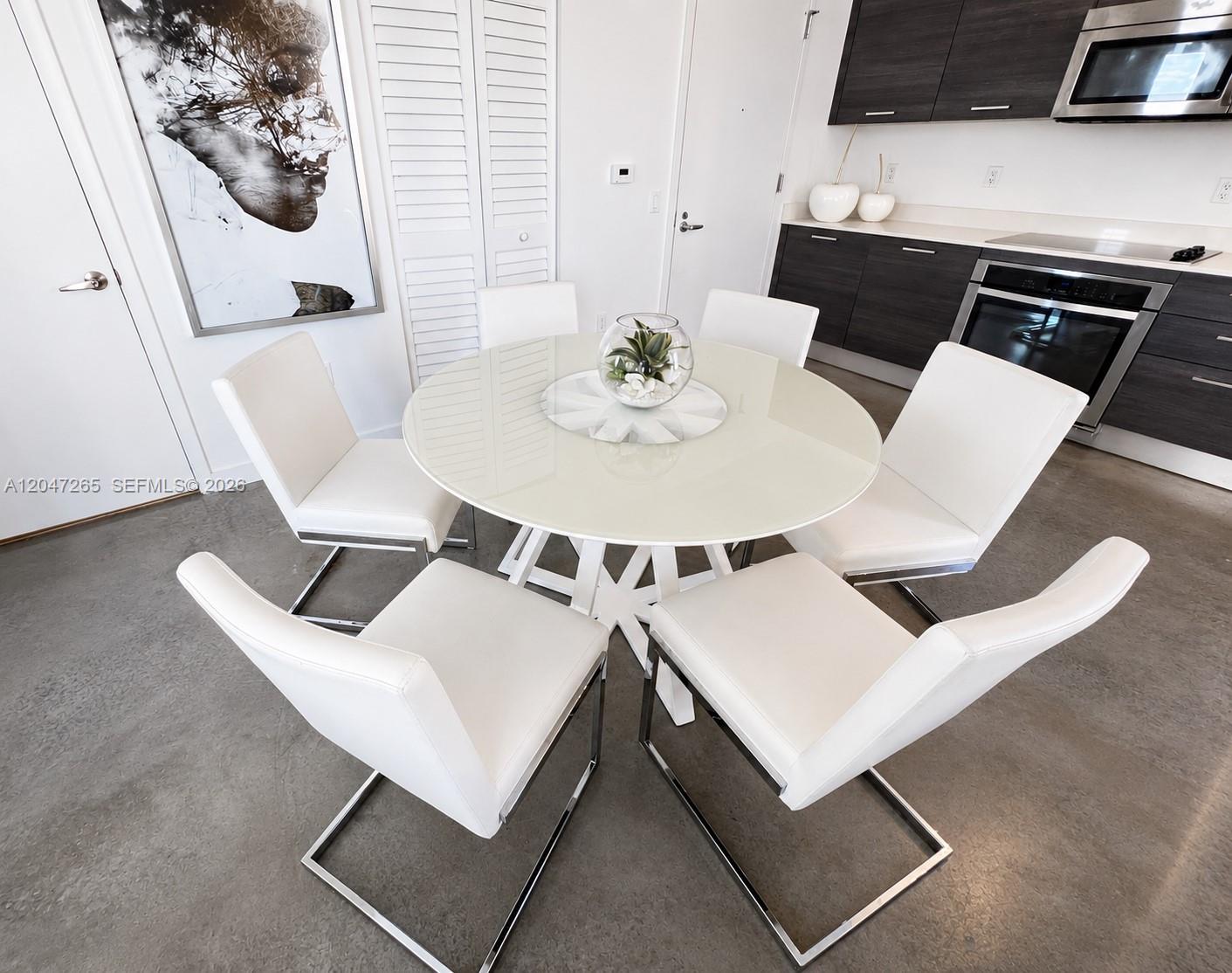 A dining area features a round glass table with five white chairs on concrete floors — 151 SE 1st St # 1602, Miami FL 33131, MIAMI, FL