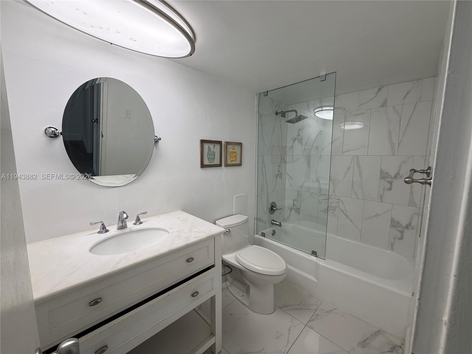 A bathroom features a white vanity, a round mirror, a toilet, and a tiled tub-shower — 5101 Collins Ave # 12K, Miami Beach FL 33140, MIAMI BEACH, FL