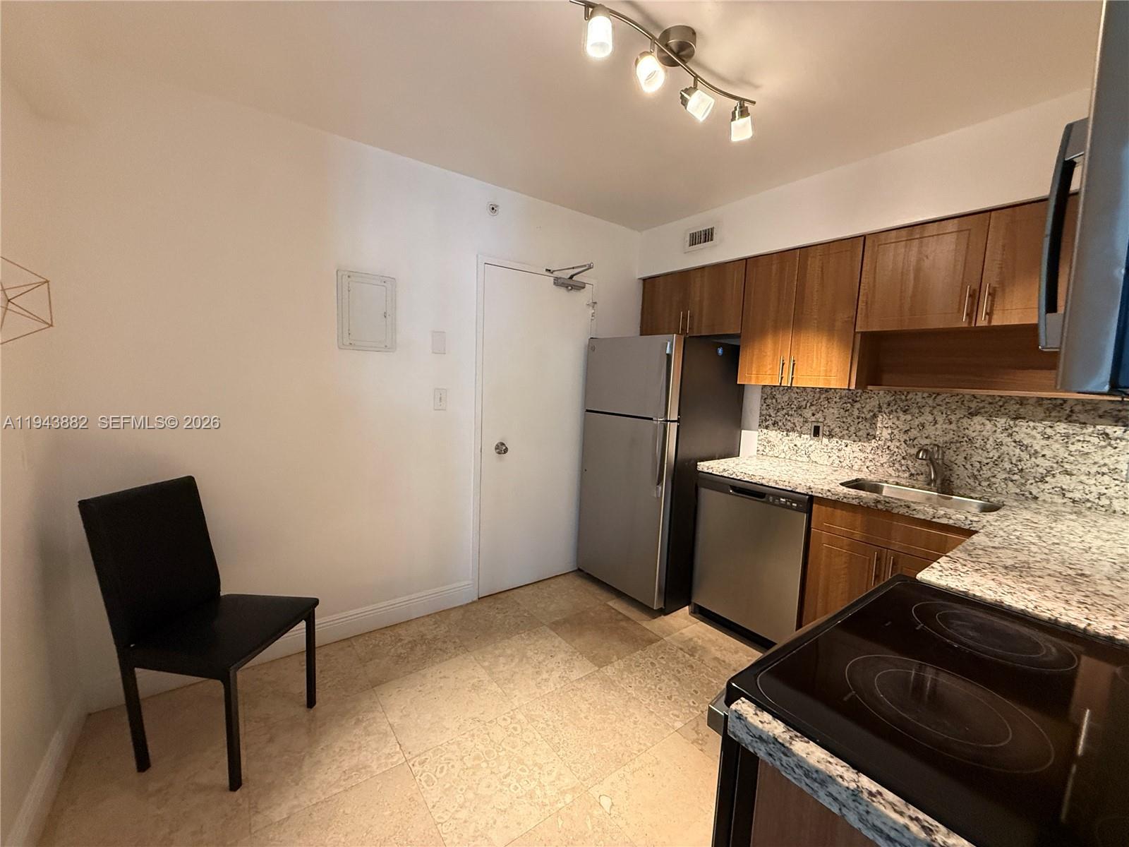 A kitchen features wood cabinets, granite countertops, stainless steel appliances, and a single black chair — 5101 Collins Ave # 12K, Miami Beach FL 33140, MIAMI BEACH, FL