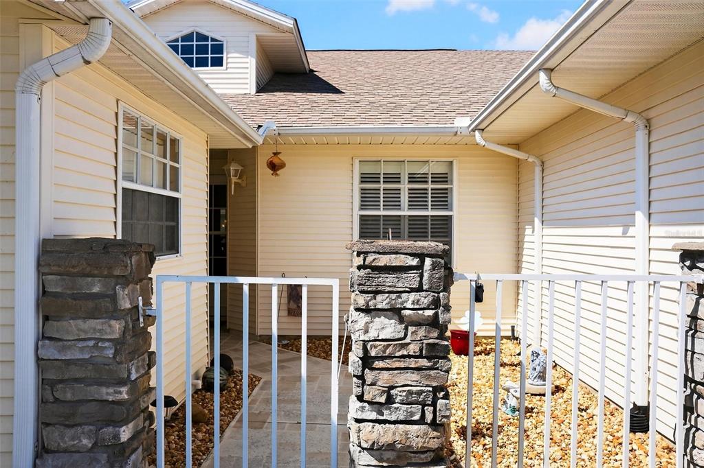 A gated stone-columned walkway leads to the entrance of a light-yellow vinyl-sided house — 26627 RACQUET CIRCLE, LEESBURG, FL
