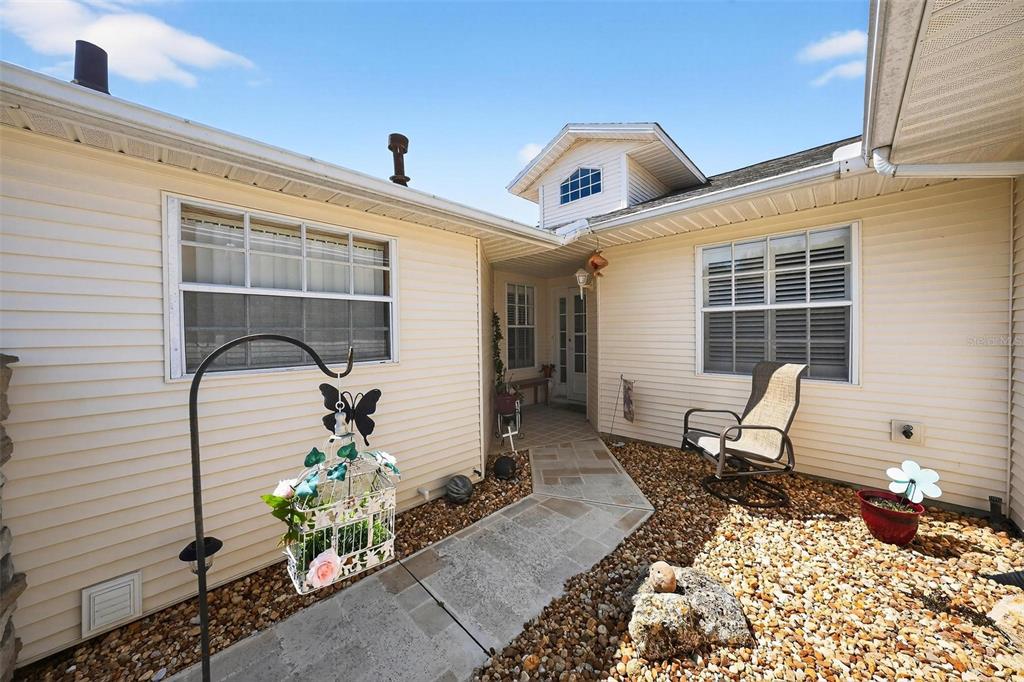 A light-colored house exterior features a stone walkway leading to a recessed front entrance — 26627 RACQUET CIRCLE, LEESBURG, FL