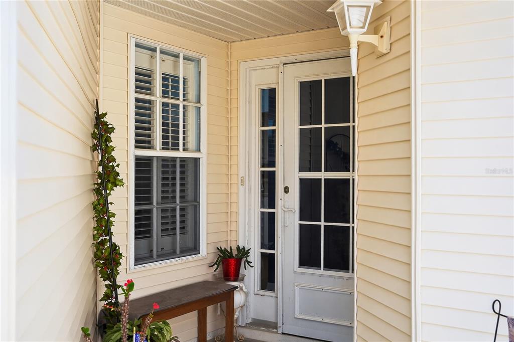 A covered front porch features light yellow siding, a white storm door, and a window — 26627 RACQUET CIRCLE, LEESBURG, FL