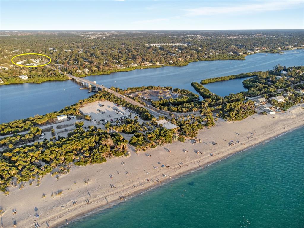 Aerial view of a beach, parking lot, and bridge with a circled house in the distance — 1730 MANASOTA BEACH ROAD UNIT 207, ENGLEWOOD, FL