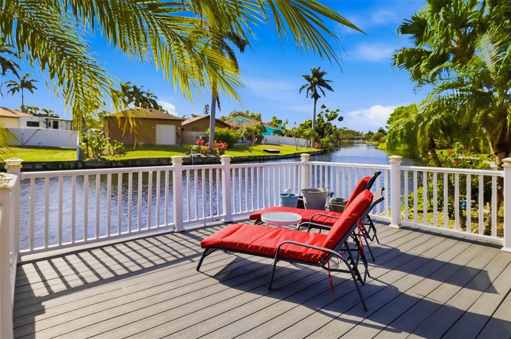 A wooden deck with two red lounge chairs overlooks a canal lined with palm trees — 1207 78TH STREET NW, BRADENTON, FL